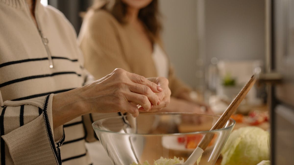 Close-up of hands preparing a fresh salad in a glass bowl within a cozy kitchen atmosphere.